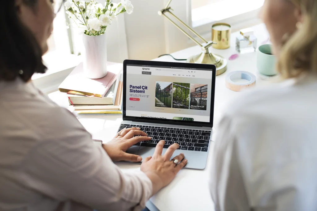 Masada iki kişi, dizüstü bilgisayarda e-ticaret mağazasının kategori sayfasını (panel çit ürünleri) inceliyor